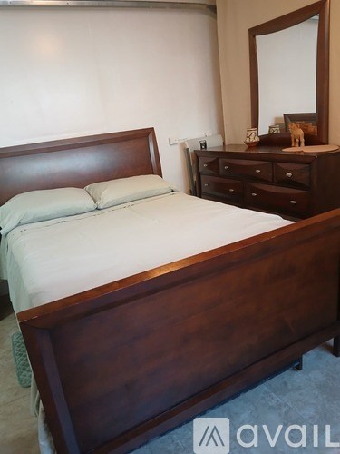 A bed with a wooden headboard and footboard sits in a room with a dresser and mirror.