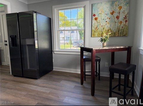 A kitchen with a black fridge, a table with two stools and a painting on the wall.