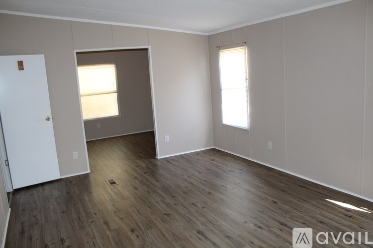 A room with wooden flooring and two windows.