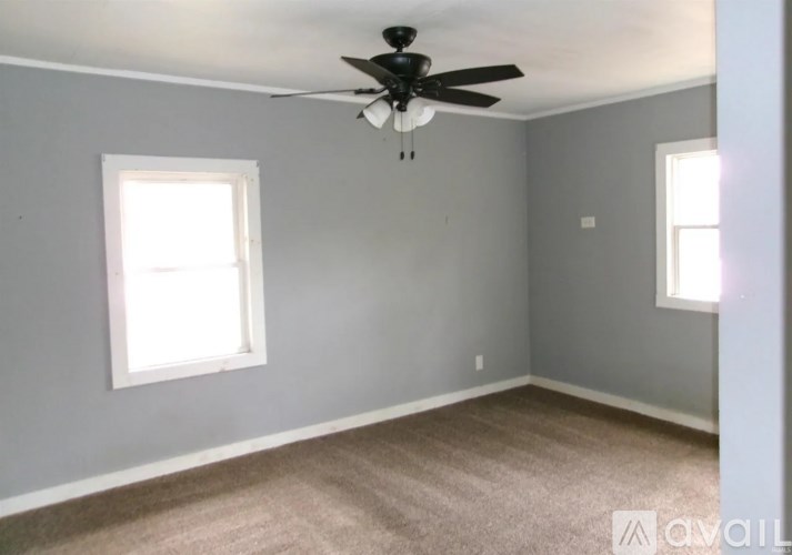 A room with a ceiling fan and two windows.