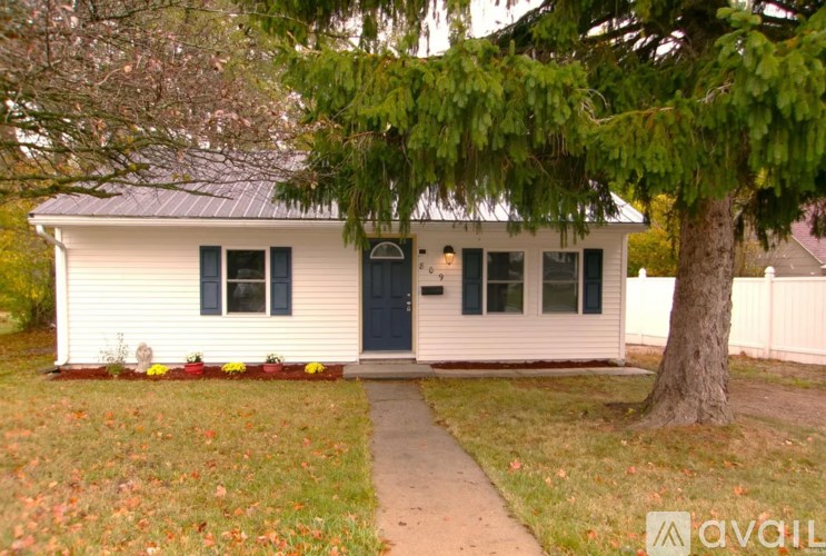 A white house with a blue door and windows is surrounded by trees and grass.