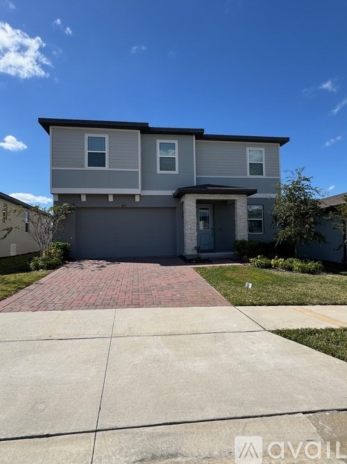 A house with a grey exterior and a red brick pathway in front.