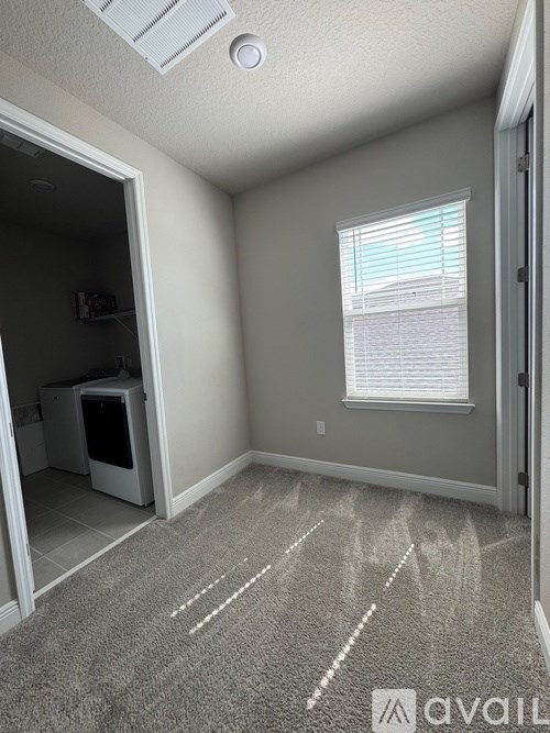 A room with a grey carpet and a white ceiling fan.