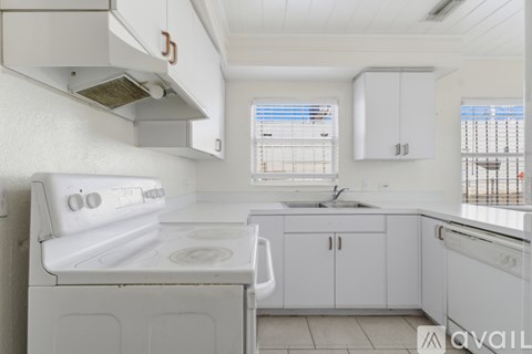 A white kitchen with a stove, sink, and cabinets.