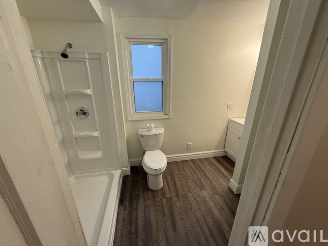 A small bathroom with a toilet, a shower, and a window.