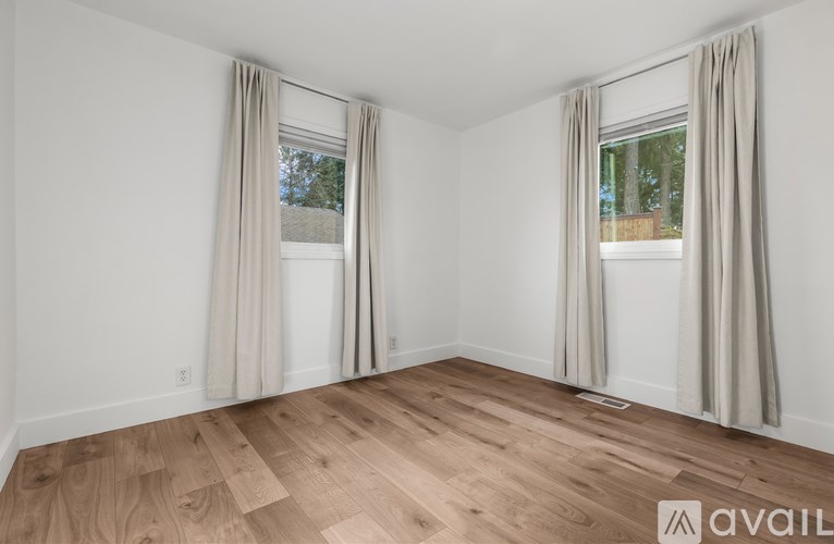 A room with wooden flooring and two windows with curtains.