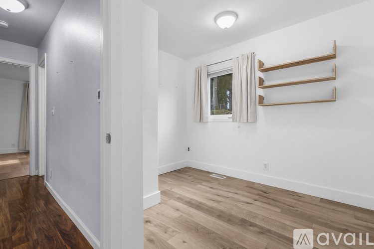 A room with white walls and wooden flooring, with a window and a coat rack.