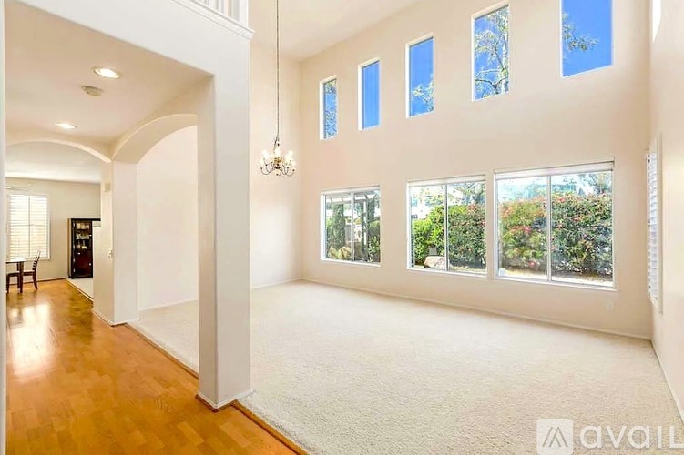 A spacious room with a chandelier, large windows, and a wooden floor.