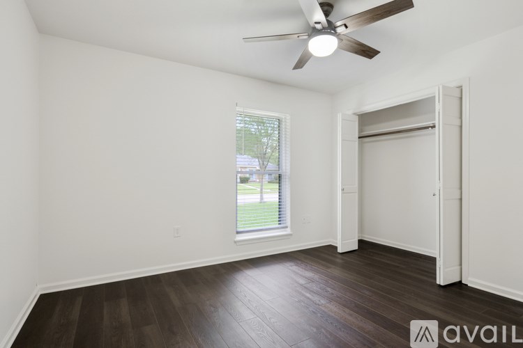 A room with a ceiling fan and a window with a view of a lawn and trees outside.