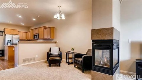 A living room with a fireplace and a kitchen area in the background.