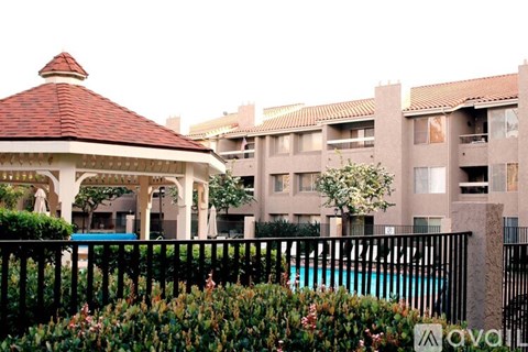 A gazebo is in front of a pool and apartment building.
