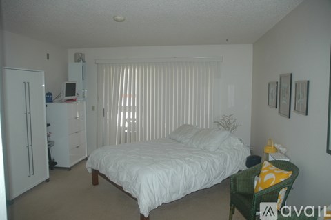 A bedroom with a bed, chair, and fridge.