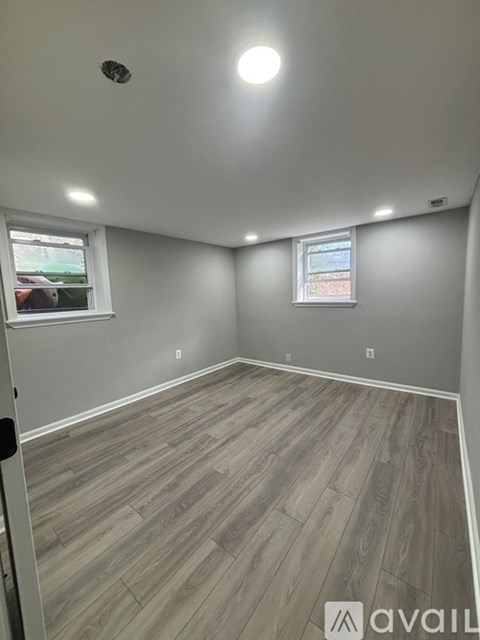 A room with wooden flooring and two windows.