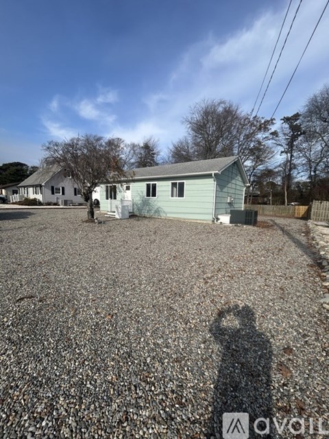 A gravel lot with a green house and a shadow of a person.