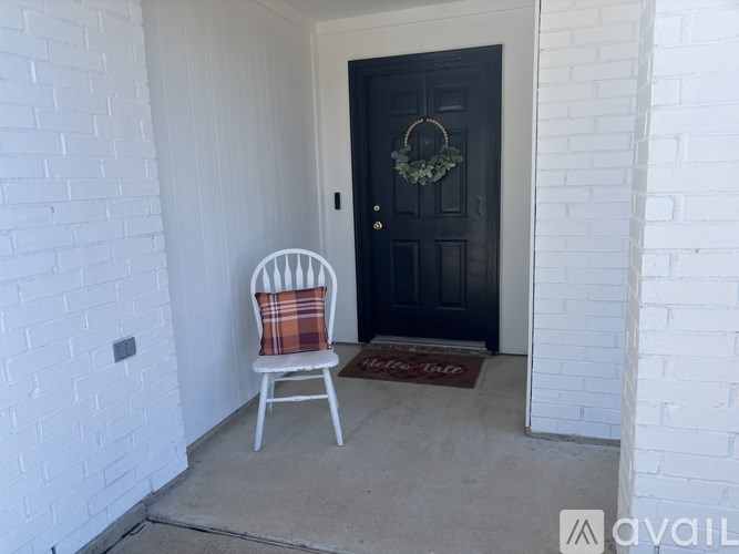 A black door with a wreath on it and a chair with a plaid blanket on it.