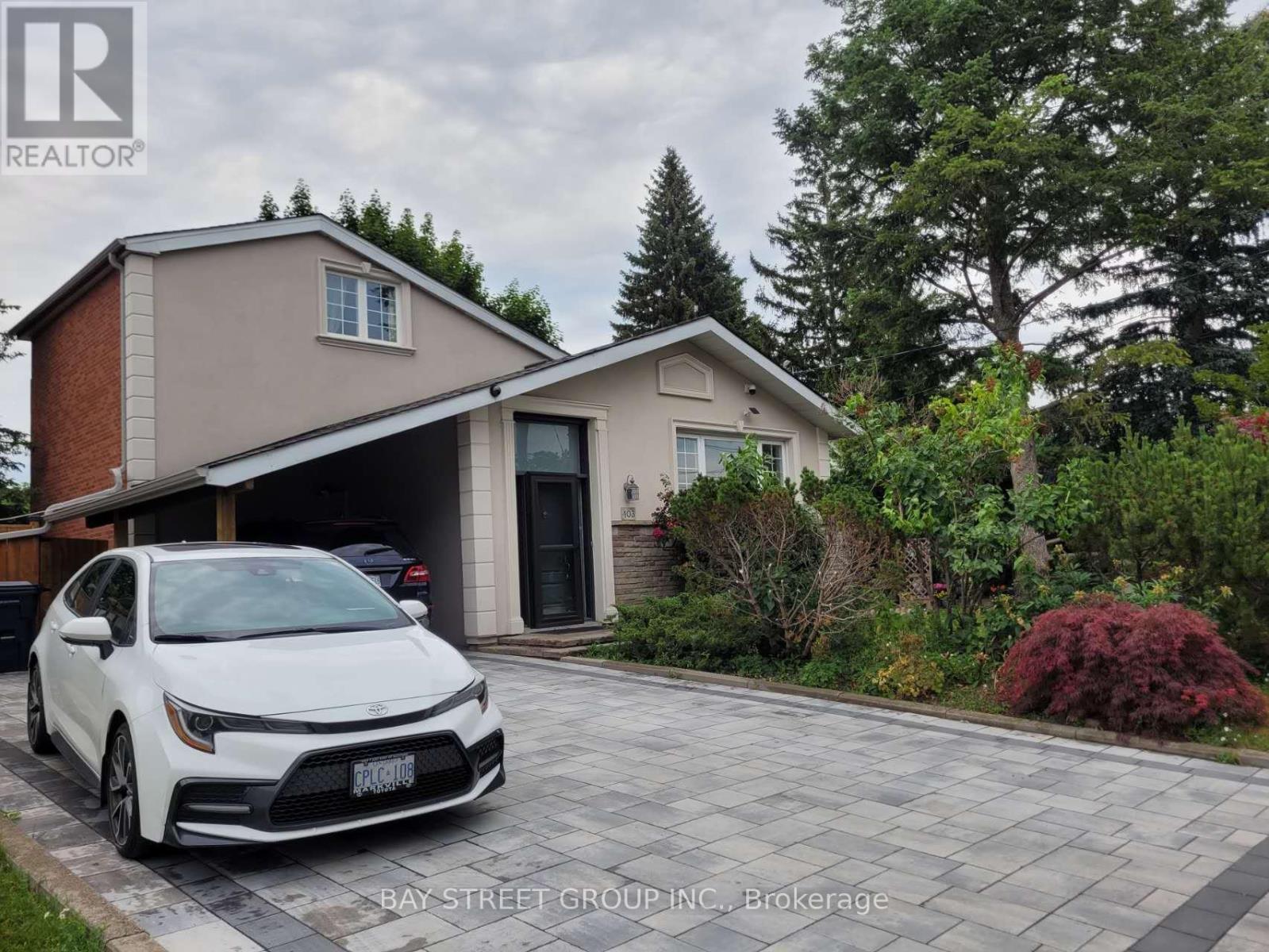 A white car is parked in front of a house with a bay window.