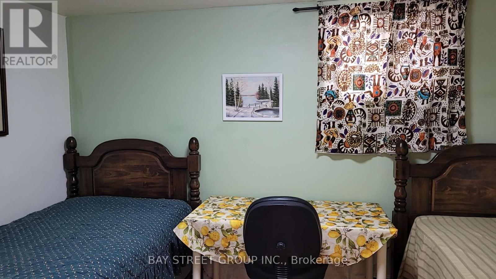 A bedroom with two beds, a table with a floral tablecloth, and a framed picture on the wall.