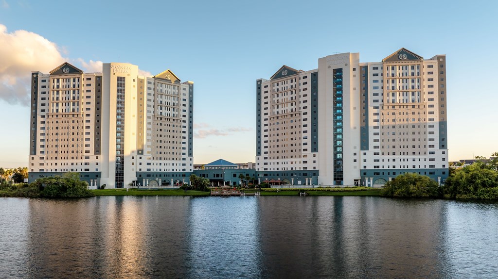 A row of modern buildings are reflected in the water in front of them.