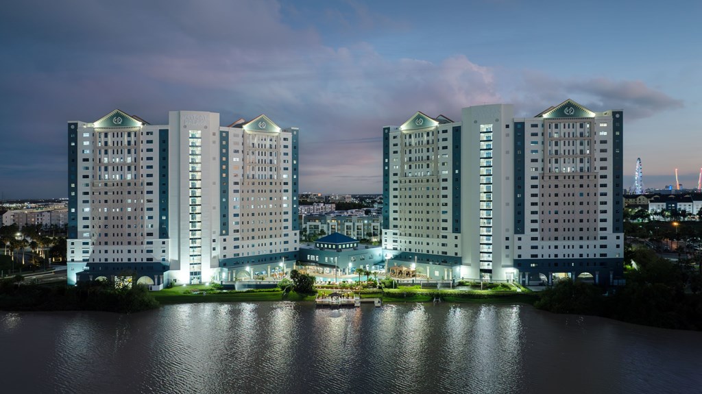 A large building complex is lit up at night with a body of water in the foreground.