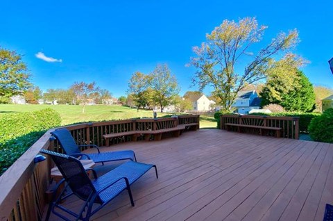 A wooden deck with chairs overlooks a grassy area and trees.