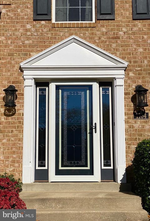 A white door with a glass panel and sidelights is set in a brick wall.