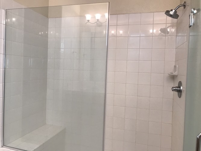 A white tiled shower with a glass door and a bench inside.