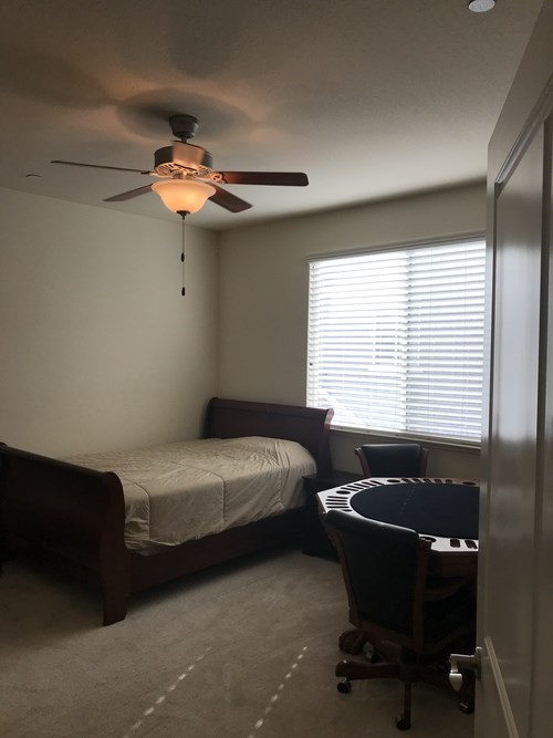 A bedroom with a bed, chair, and a ceiling fan.