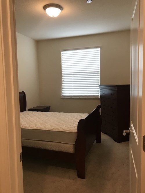 A bedroom with a bed, dresser, and window with blinds.