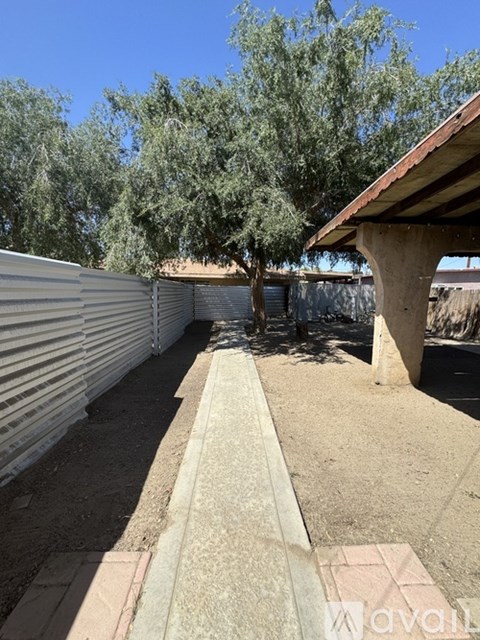 A concrete walkway leads through a shaded area with trees.