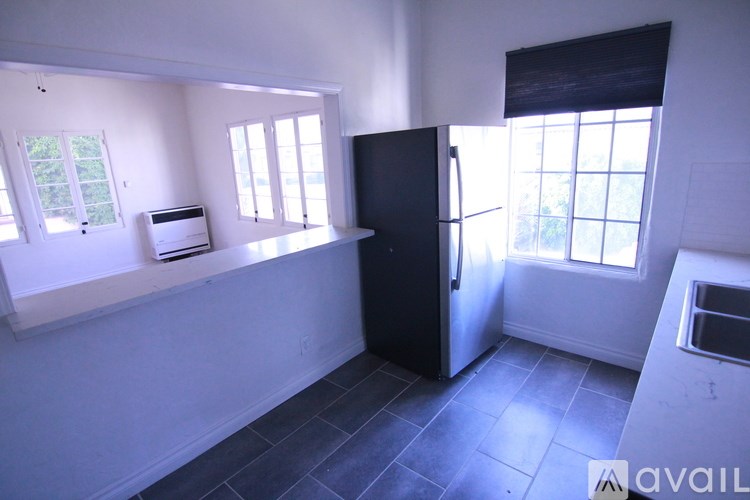 A kitchen with a black fridge and a window with blinds.