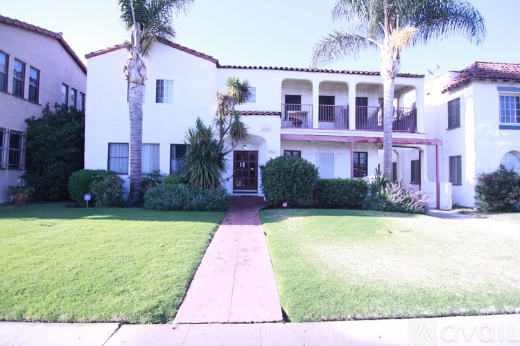 A white two-story house with a red roof and a balcony on the second floor.