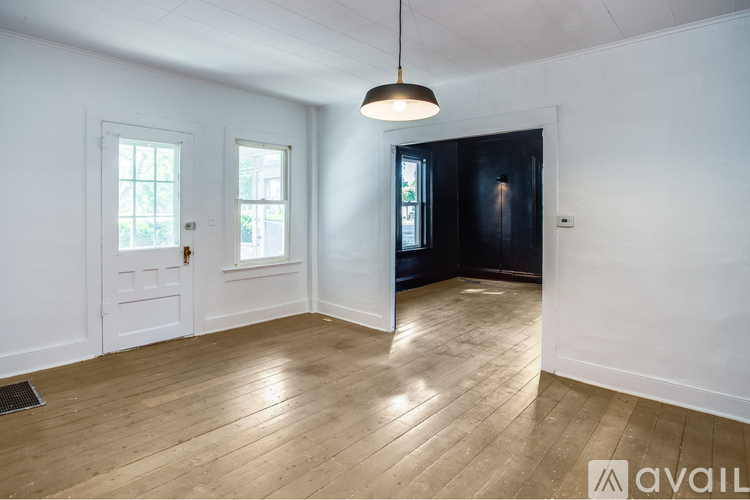 A room with wooden flooring and white walls, with a black door and two windows.