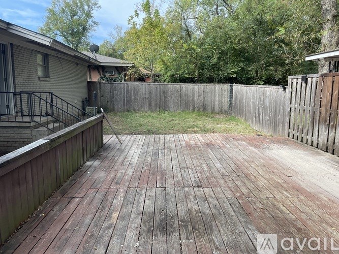 A wooden deck in a backyard with a fence and trees in the background.