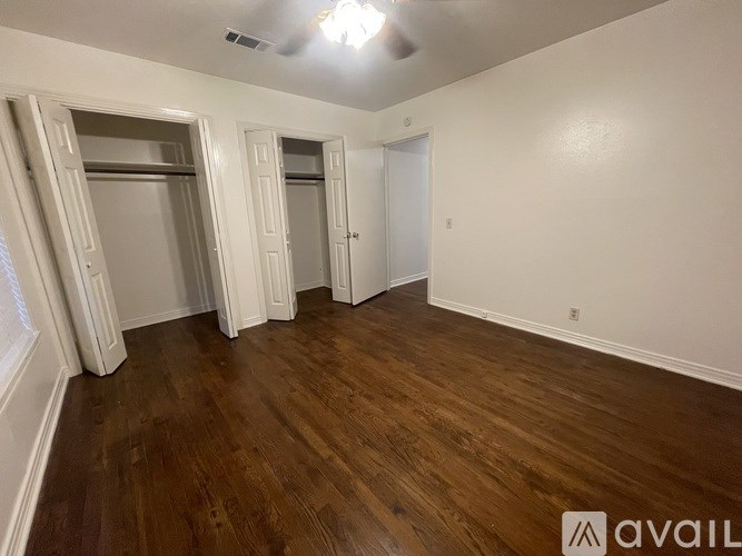 A room with wooden flooring and white walls, with a window on the left side.