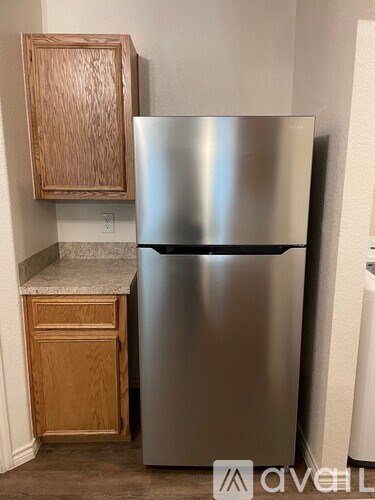 A stainless steel refrigerator stands next to a wooden cabinet in a kitchen.