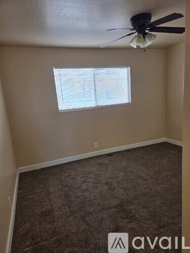 A room with a carpeted floor, a ceiling fan, and a window with blinds.