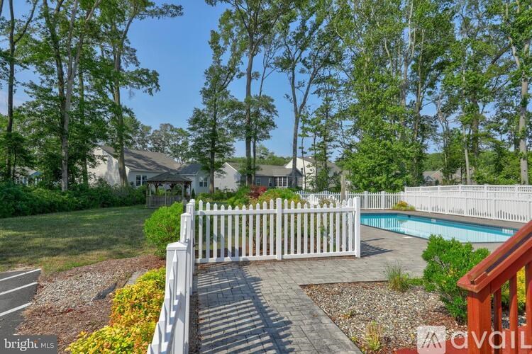 A white picket fence leads to a pool surrounded by trees.