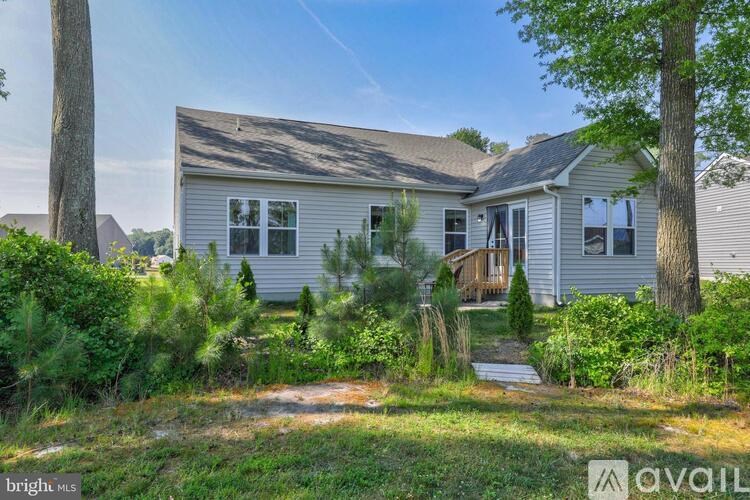 A house with a grey siding and a brown roof is surrounded by greenery.