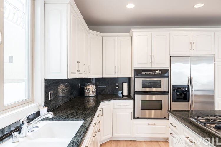 A modern kitchen with white cabinets and black countertops.