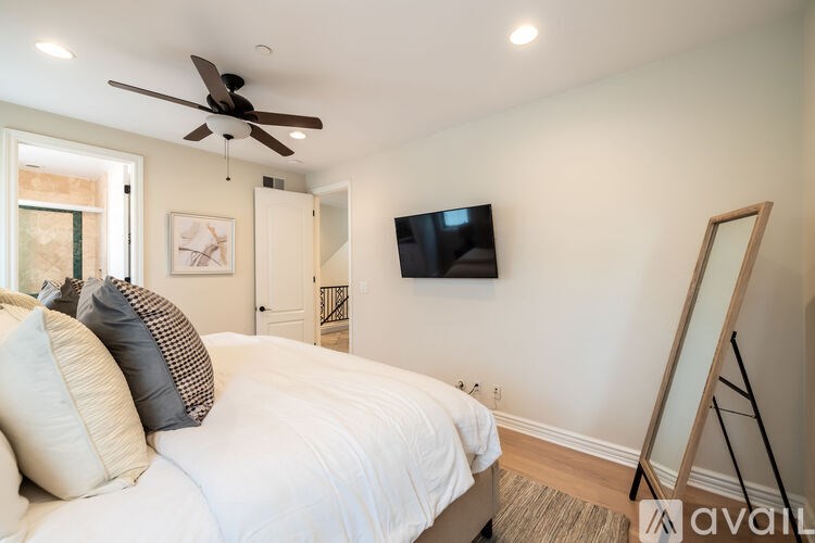 A bedroom with a bed, a ceiling fan, a flat screen TV, and a painting on the wall.