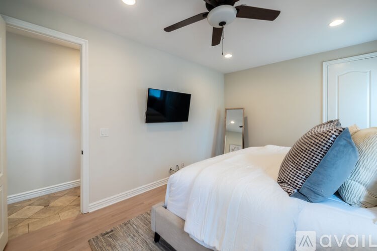 A bedroom with a bed, a ceiling fan, and a flat-screen TV mounted on the wall.