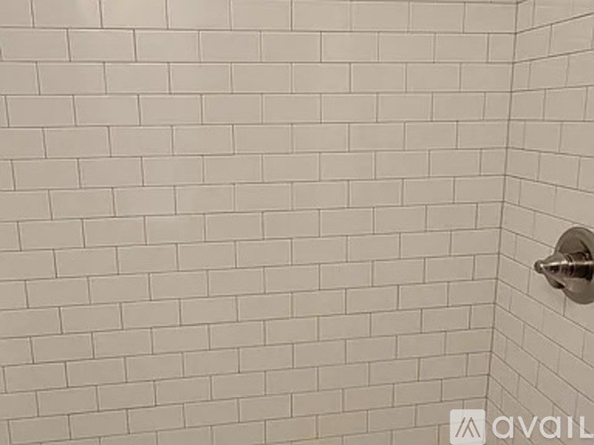A white tiled shower wall with a silver faucet.