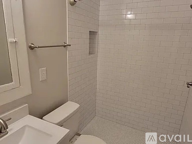 A white tiled bathroom with a toilet, sink, and shower.