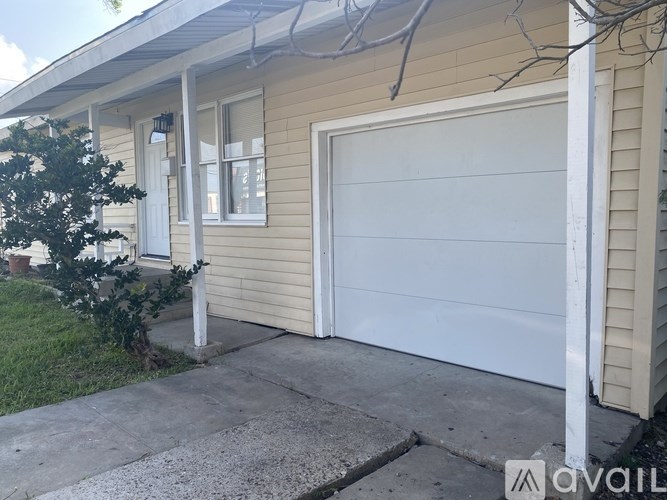 A beige house with a white garage door and a small tree in front.