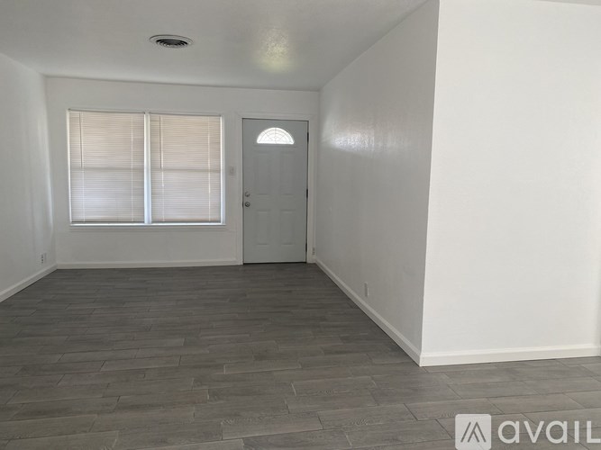 A room with a grey floor and white walls has a door and a window with blinds.