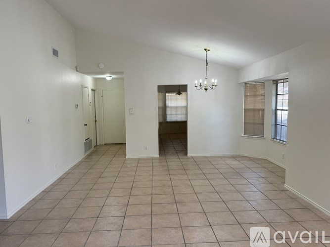 A spacious room with tiled flooring and a chandelier hanging from the ceiling.