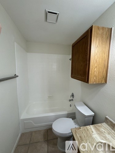 A small bathroom with a toilet, tub, and wooden cabinet.