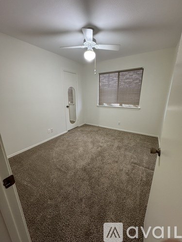 A room with a carpeted floor, a ceiling fan, and a window with blinds.