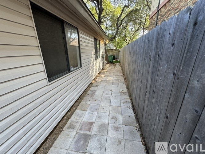 A long, narrow alleyway with a wooden fence on one side and a house with a window on the other.