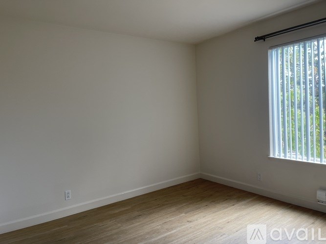 A room with a window covered by blinds and wooden flooring.